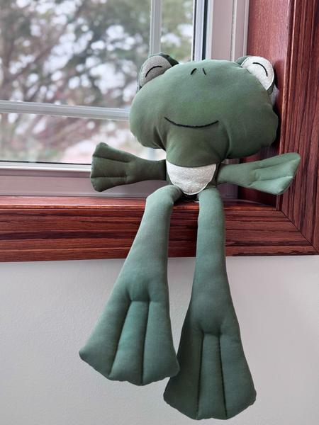 happy frog plush toy sitting in window sill