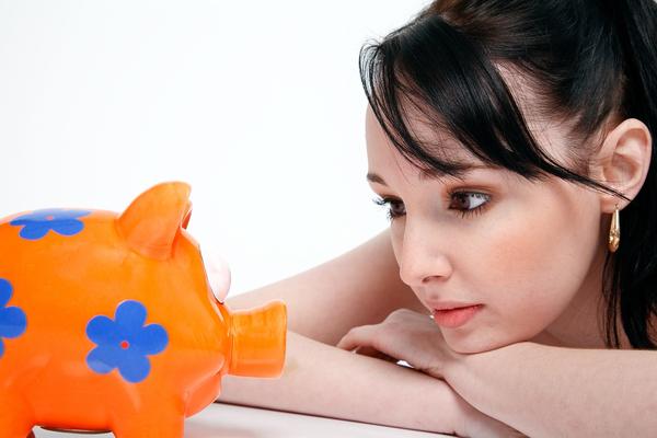 image of a woman staring sadly at an orange piggy bank with blue flowers