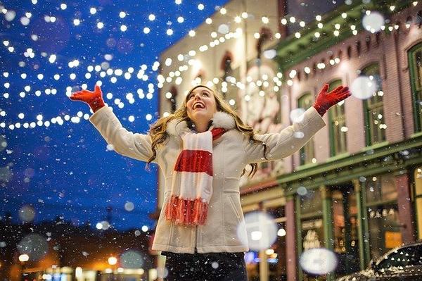 image of woman wearing scarf and gloves looking happily at holiday lights in street