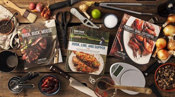 Three cookbooks on a table full of kitchen tools and ingredients