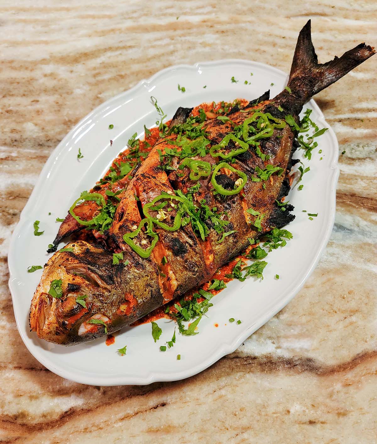 Grilled pompano with herbs and chiles on a plate. 