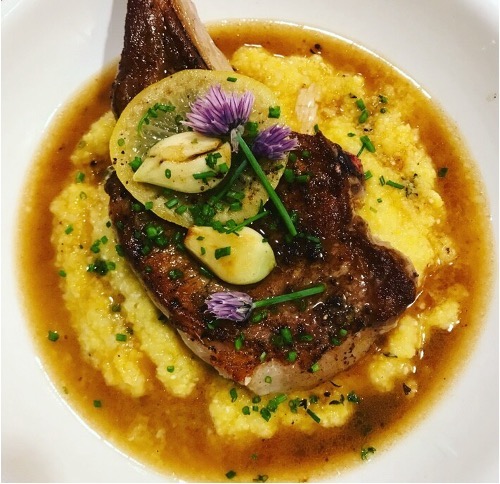 Bone-in pork chop over creamy polenta with pan sauce, chives and chive blossoms, plated by a private chef in Bucks County