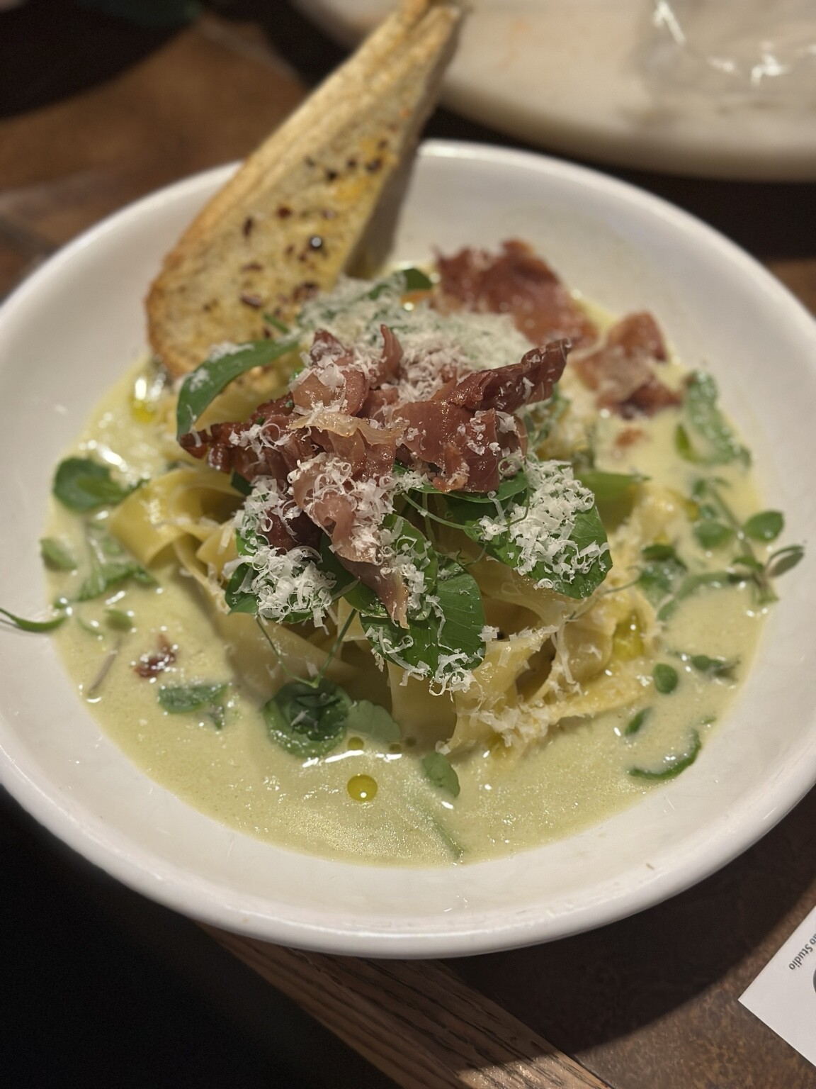 Fresh tagliatelle in a creamy herb sauce with crispy prosciutto, grated cheese and grilled bread