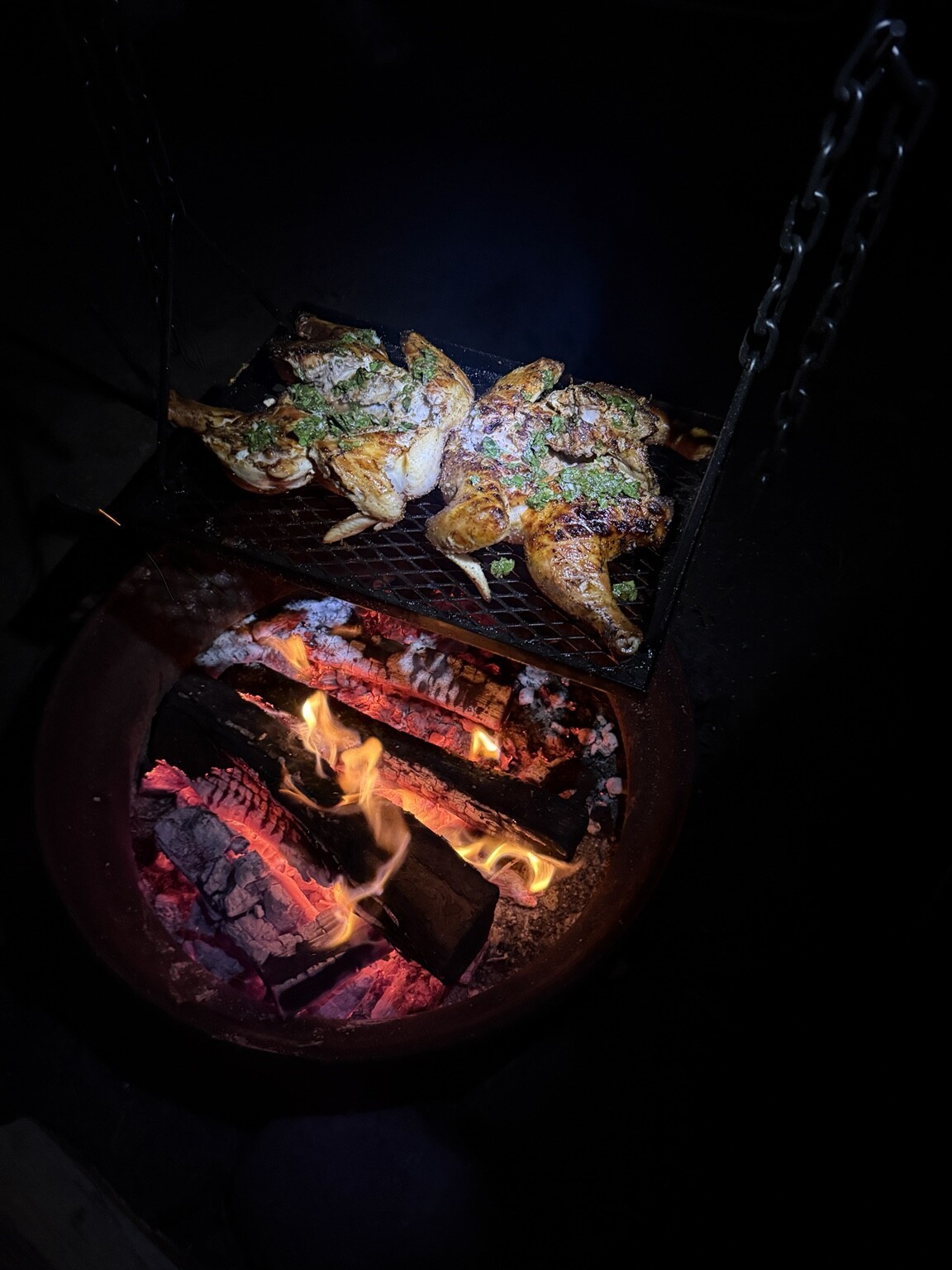 Spatchcocked chicken with herb sauce cooking over an open wood fire