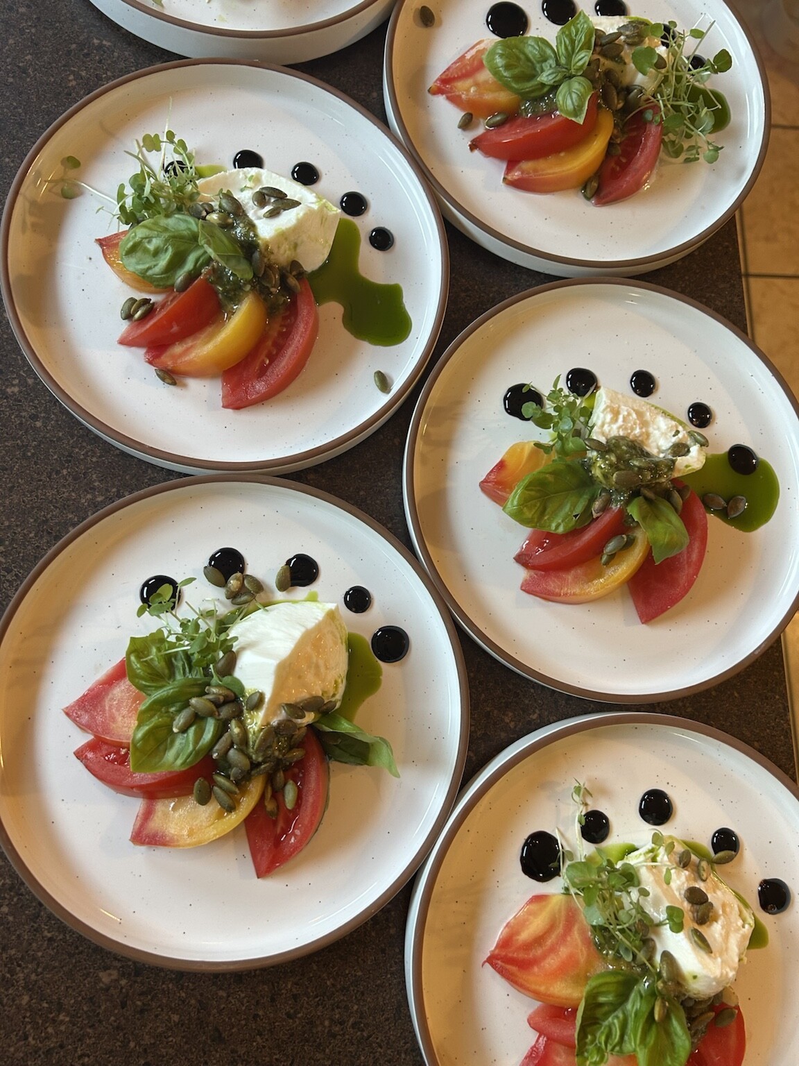 Multiple plates of heirloom tomato and burrata caprese with basil, pumpkin seeds and balsamic, plated by a private chef in Bucks County