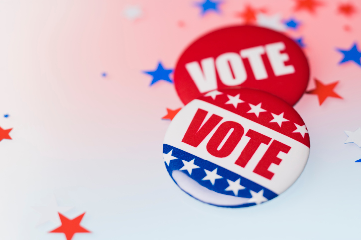 Image of two buttons that say VOTE laying on a white background with blue, white, and red star confetti