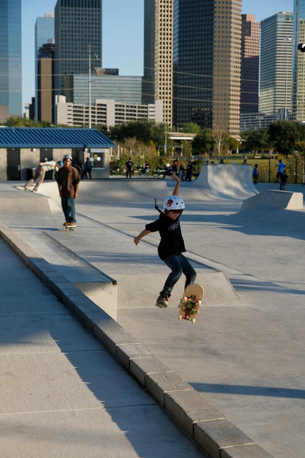 Image - Young skateboarder flings his arms to balance, Houston, Texas skyline behind, Lee & Joe Jamail Skatepark, © Heidi Straube 2013